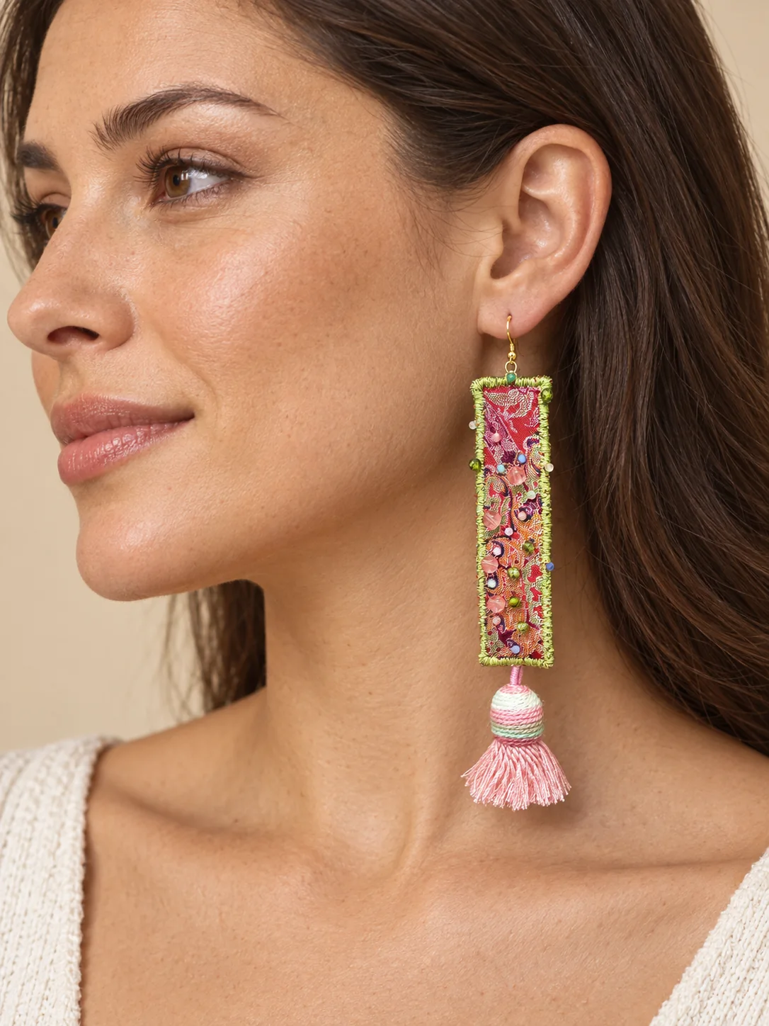 Close view of a pink tassel textile earring worn beside the model's neck.