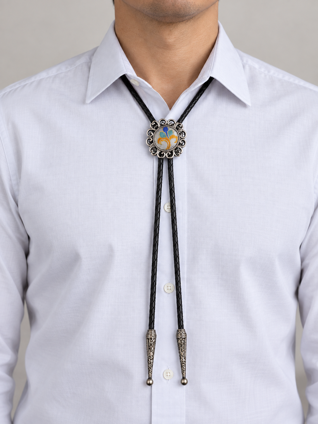 Adult model wearing the multicolor circular bolo tie with black braided cord and two long engraved silver-color tips.