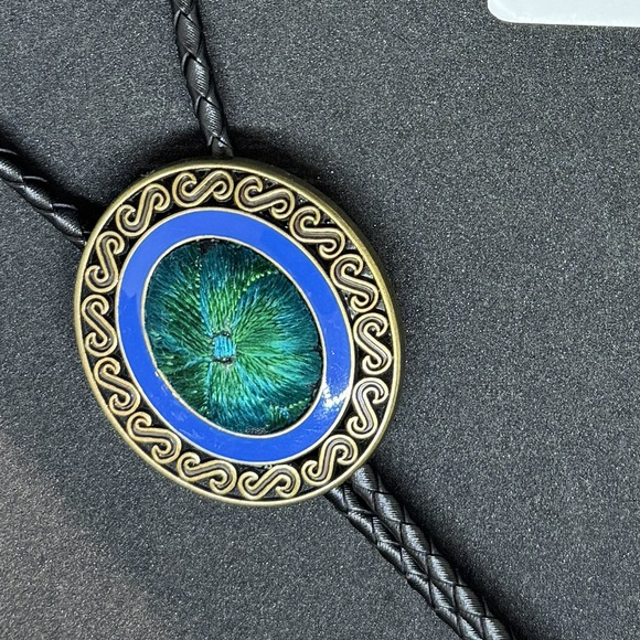 Close view of the blue ring and green patterned center in an antique-bronze-color oval scroll frame.