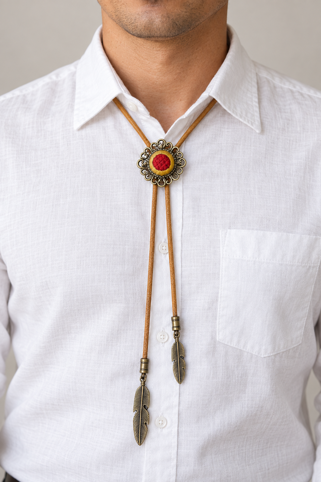 Adult model wearing the red-and-mustard patterned bolo tie with tan cord and unequal feather-shaped tips over a white shirt.