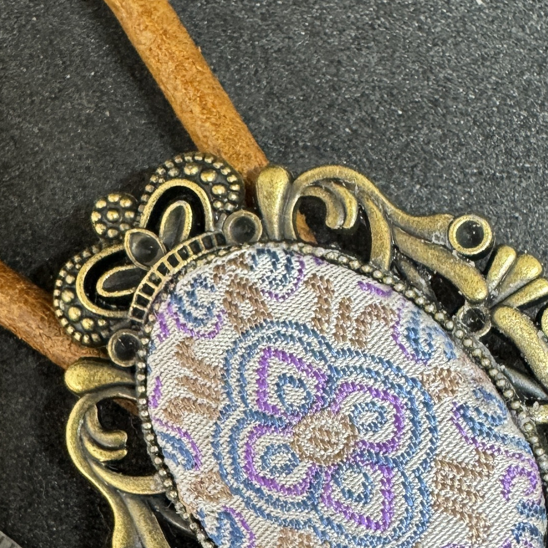 Close view of the pale blue, lavender, and beige woven center in an antique-brass-color oval frame.