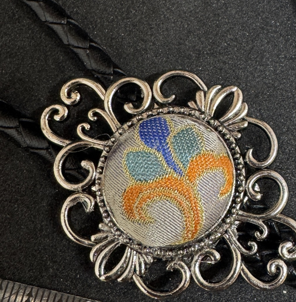 Close view of the orange, blue, green, and beige woven center in a silver-color circular frame.