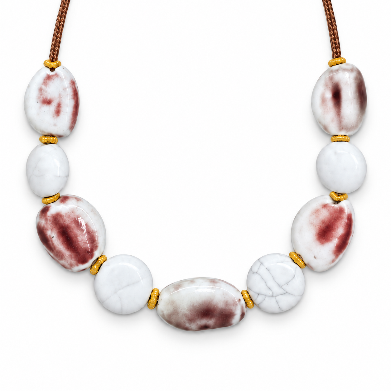 Close-up of nine pale, maroon-blushed and crackle-pattern ceramic beads with gold-color spacers.